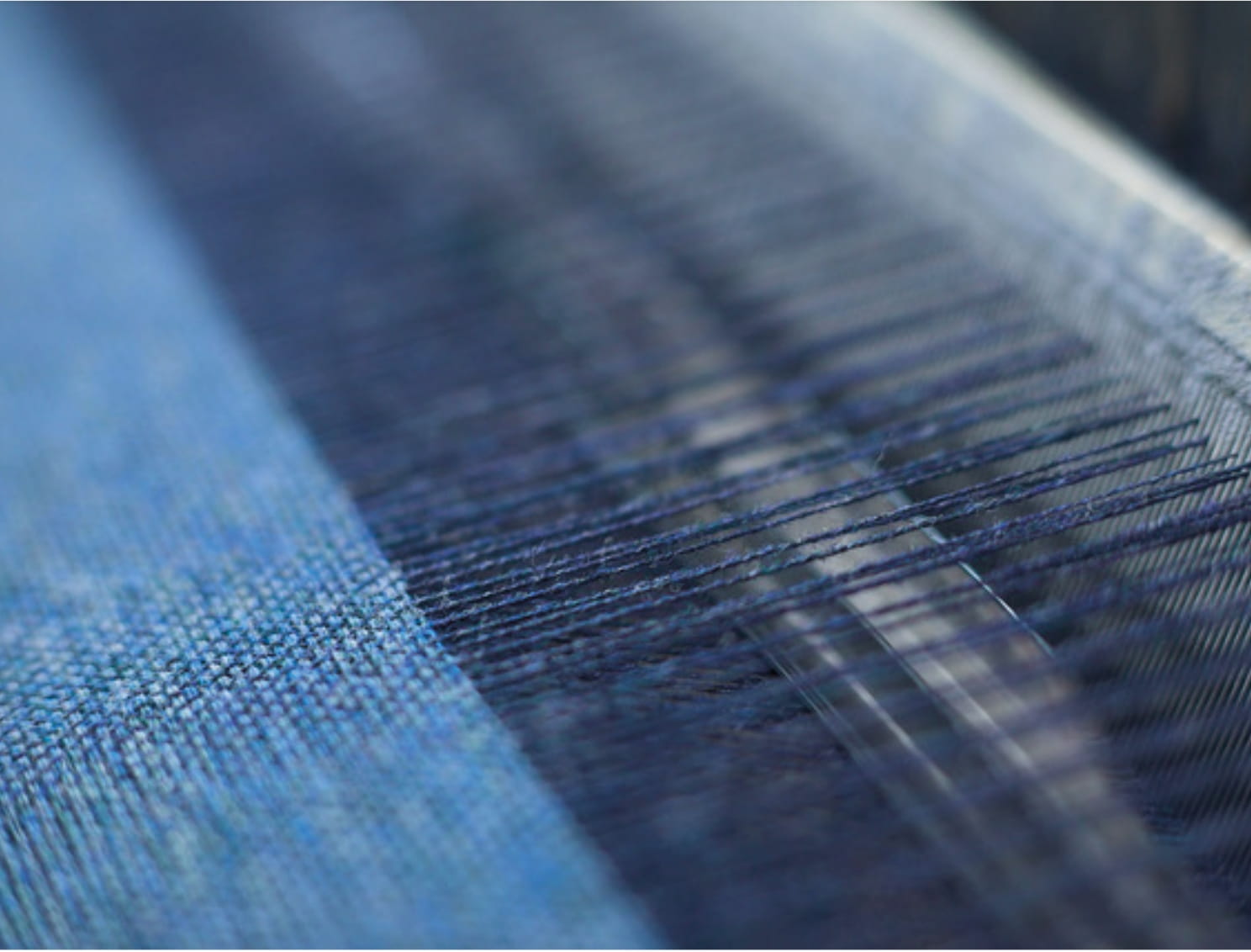 Close-up of a weaving process with blue yarns and fine textile structure as an example of high-quality fabric processing and textile design by Die Stoffmacher in Stuttgart, Baden-Württemberg.